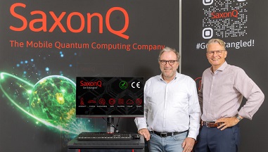 Marius Grundmann, CEO von SaxonQ steht mit einer weiteren Person vor einer Messewand, darauf der Text: SaxonG, The Mobile Quantum Computing Company