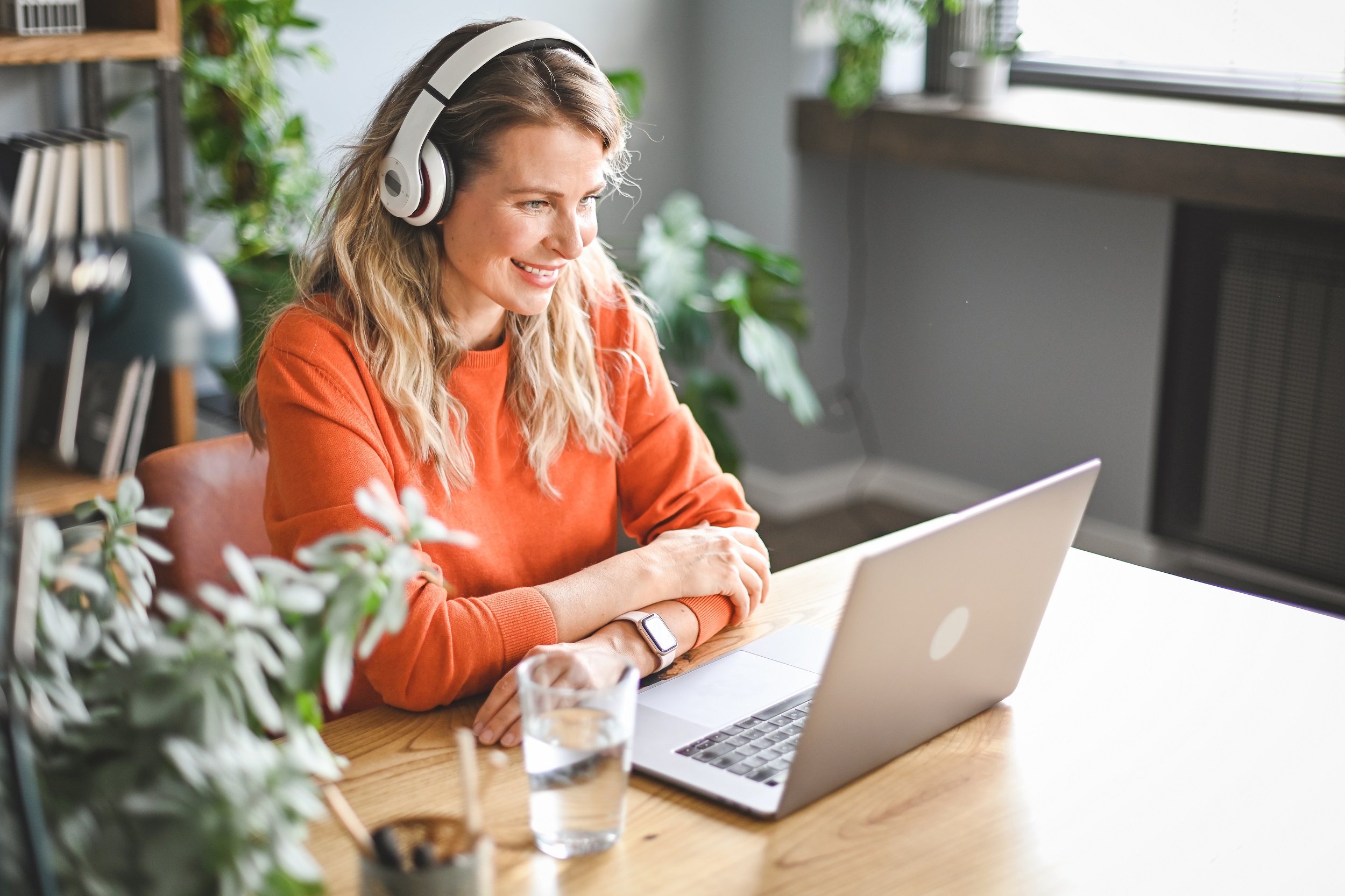 Frau sitzt am Schreibtisch vor ihrem Laptop und hat ein Headset auf.