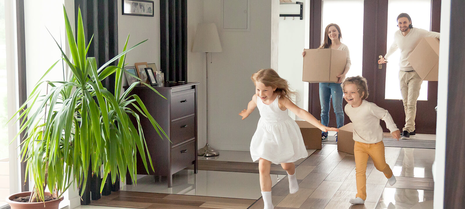 Symbolbild zum Thema Wohnen: Eine Familie betritt mit Umzugskartons ihr neues Haus, zwei Kinder rennen vorweg.