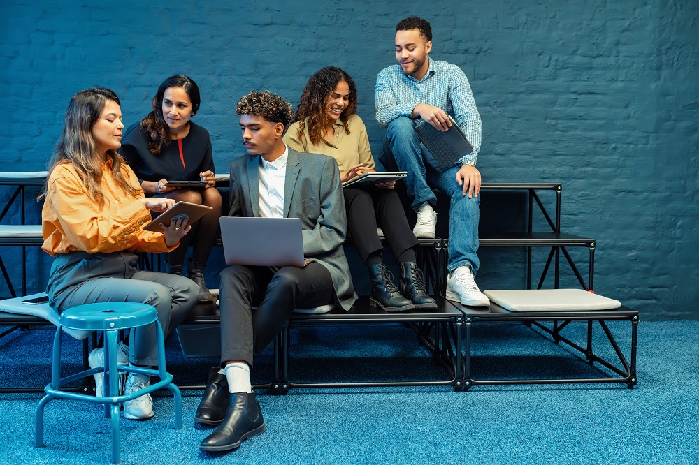 5 Menschen sitzen in einer modernen Bürolandschaft und unterhalten sich